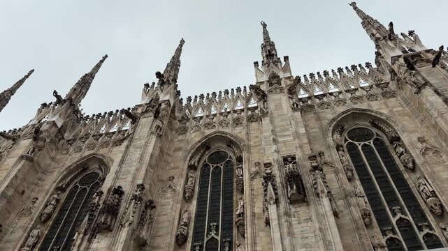 Milan, Italy - May 05, 2026: Milan Cathedral features detailed Gothic design with spires and statues, framed by pink roses in a city square setting