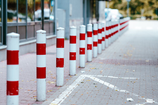 Striped metal bollards standing along a paved urban sidewalk on a bright afternoon