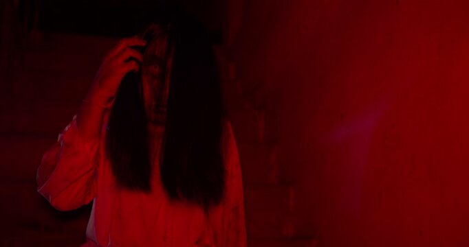 A terrifying female ghost emerges from the shadows of a dark, red-lit basement, creating a suspenseful and scary scene perfect for a Halloween horror movie trailer.