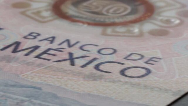 Macro view of a Mexican peso banknote showing Banco de Mexico text, intricate security patterns, printed details, and colorful currency design in Mexico.