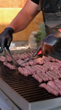 Traditional Balkan cevapi made from minced meat being grilled on a hot barbecue. Close-up of a cook preparing ćevapi at an outdoor food stall.