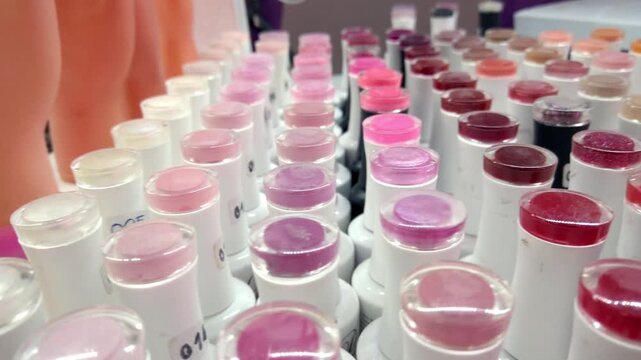 Macro close up of multiple cosmetic lipstick samples in white tubes arranged in rows, displaying pink, red, purple, and translucent shades for beauty product testing
