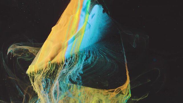 Close-up view of thick yellow and cyan pigments moving over angular translucent plane suspended in dark liquid, with paint, pigment, liquid, fluid detail