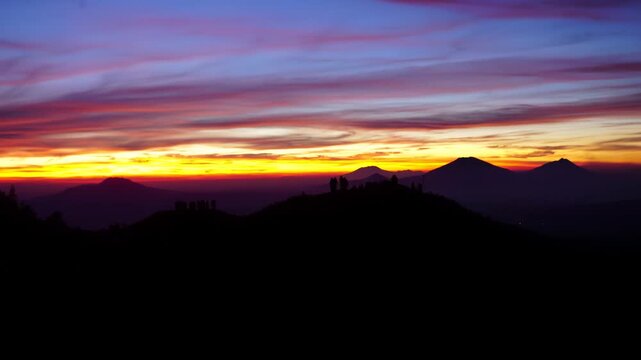 Sunrise over Volcanic Peaks in Central Java: Silhouetted Hikers on Hilltop at Dawn