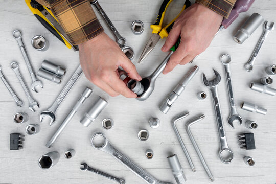 A top view of hands assembling a ratchet and socket wrench among a set of metal hand tools. Concept for professional repair, construction, and maintenance.
