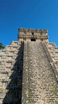 El Castillo Mayan pyramid at Chichen Itza stands under a clear blue sky as the camera tilts up along the ancient stone staircase in Mexico.