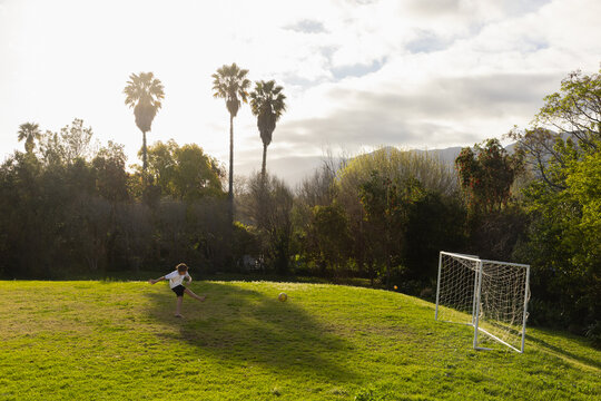 teenage boy playing with soccer ball in late afternoon light on field with palm trees in background