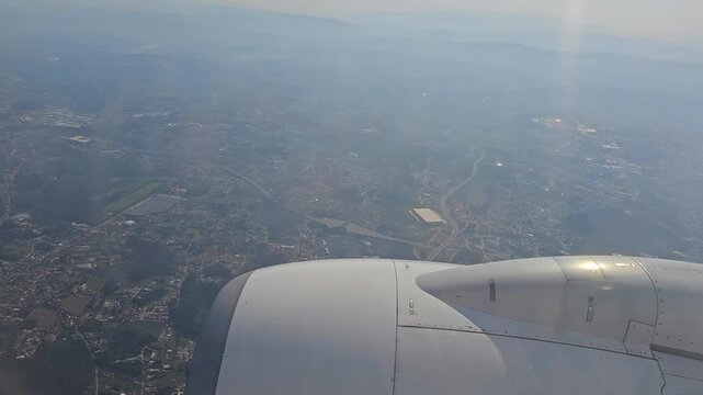 Passenger views wing during flight over city. Hazy sky above sprawling urban landscape. Engine nacelle prominent in foreground. View from high altitude, slightly blurred. Ideal for travel, journey