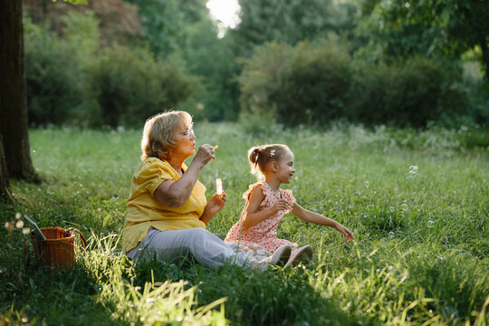 Grandmother and granddaughter blowing bubbles in park