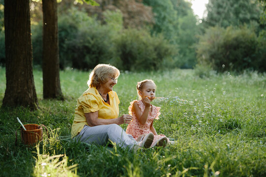 Grandmother watching granddaughter blowing bubbles in park