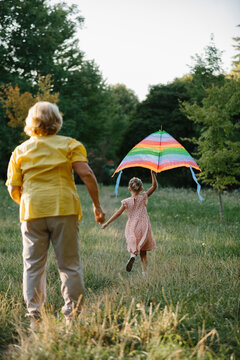 Grandmother holding granddaughter's hand, flying kite in park