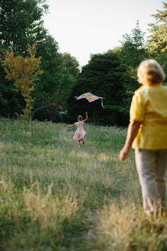 Granddaughter running with kite while grandmother watches