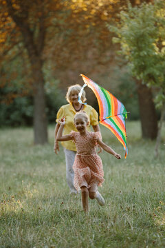 Happy granddaughter playing with kite, grandmother watching in park