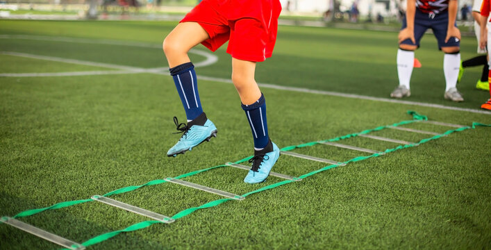Selective focus to soccer players legs and feet running through an agility ladder during outdoor training on a green turf field, enhancing footwork.