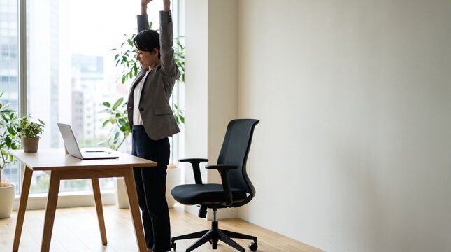 Businesswoman stretching during a work break in a bright, contemporary office space with laptop and plants.