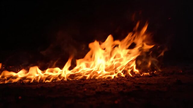 Close up of a vibrant campfire burning at night with embers and sparks flying upwards in slow motion