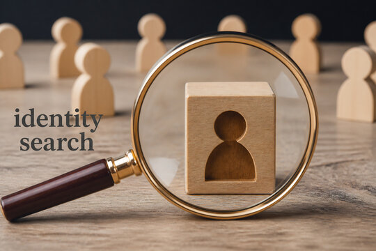 A magnifying glass focuses on a wooden person icon on a wooden surface, symbolizing identity search.