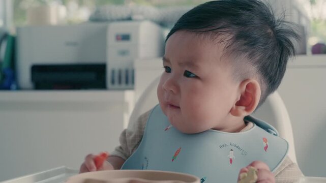 Asian baby boy self feeding sweet corn using baby led weaning method at home.	

