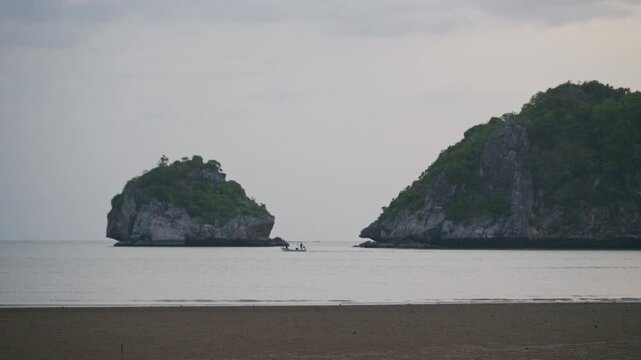 Small fishing boat sailing between limestone islands on calm sea.