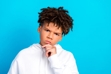 Thoughtful teen boy portrait in white hoodie looking pensive against bright blue background,...