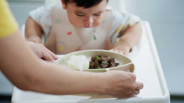 Asian baby boy self feeding sweet corn using baby led weaning method at home.	
