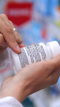 Pharmacist wearing a white coat attentively reads the instructions and ingredients on a white pill bottle label, carefully checking the dosage information before dispensing the medication