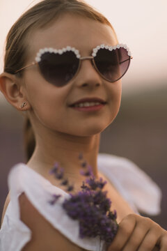 Lavender sprigs held by young girl wearing heart shaped sunglasses during golden hour outdoor portrait session
