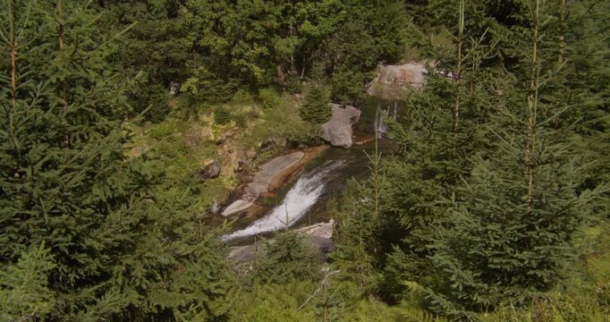 A highangle shot of a small waterfall flowing through a rocky creek surrounded by dense pine trees in the Bohemian Paradise region. Captures themes of sustainability and wellness.