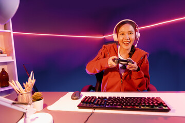 Host channel of smiling beautiful Asian girl streamer with joystick playing online game wearing headphones paste talking with viewers media online. Esport skilled team players in neon room. Stratagem. © InfiniteFlow