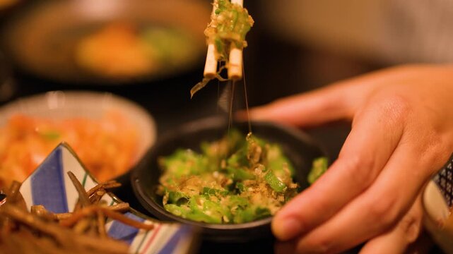 Person Eating Japanese Okra Salad with Chopsticks in Restaurant