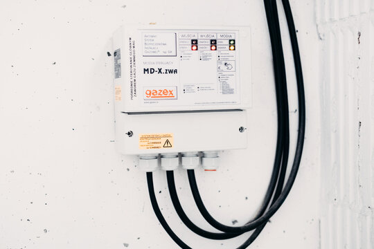 Wall mounted gas detection control module with indicator lights, cable glands and Polish warning label on white wall. Gas leak detection systems, building safety. Warsaw, Poland, 20 March 2026.