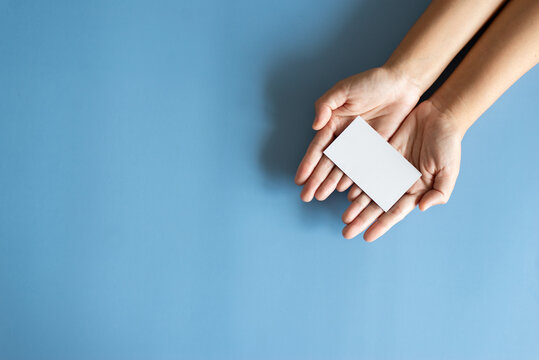Overhead view of hands holding blank white business card on blue background