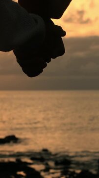 Silhouette of a romantic couple holding hands and caressing each other's fingers, symbolizing love and togetherness against a beautiful golden hour sunset over the calm sea