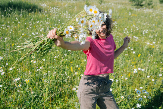 A woman holds a bouquet of daisies in a sunny summer meadow