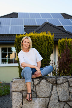 Woman sitting on stone fence in front of house with solar panels