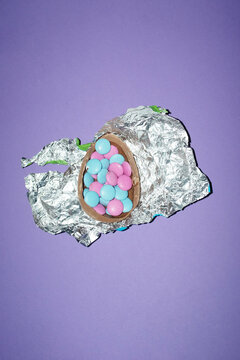 A broken chocolate easter egg holds colorful candy on silver foil