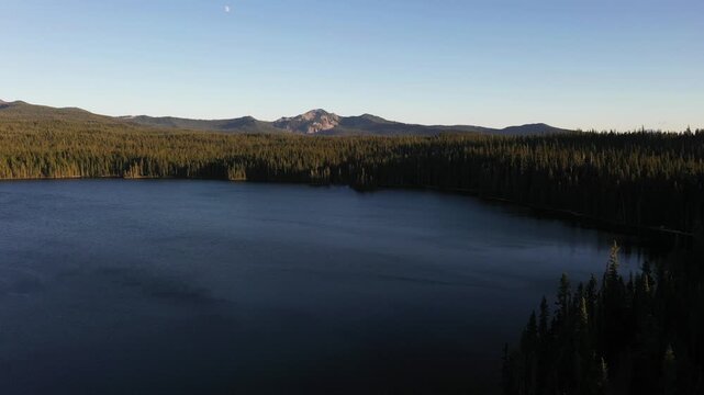 4K aerial drone footage of Summit Lake near Diamond Peak Wilderness, Oregon, USA, at sunset on a clear late summer evening, surrounded by dense evergreen forest in the Cascade Mountains