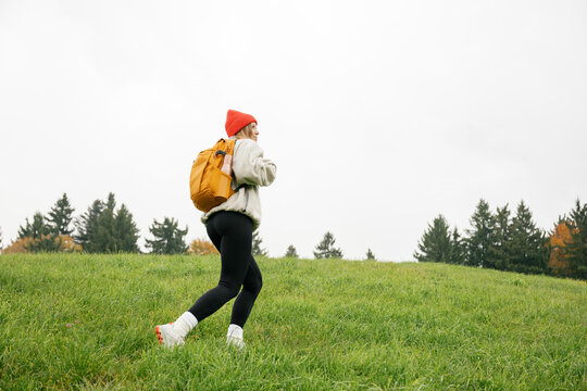 A woman with a backpack hikes through a green mountain meadow