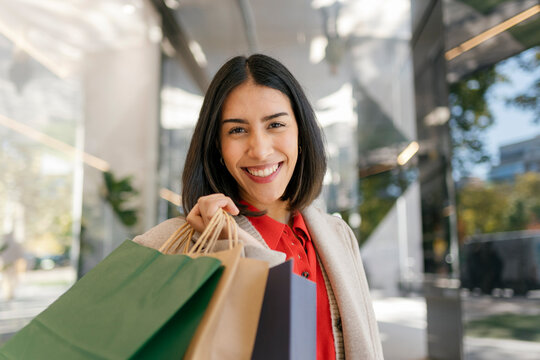 A smiling young woman holds paper bags after shopping in the city