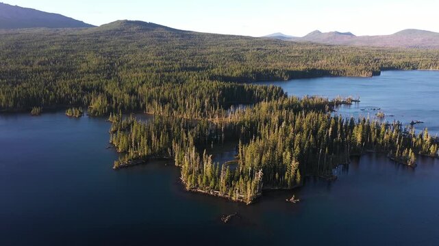 4K aerial drone footage of Summit Lake near Diamond Peak Wilderness, Oregon, USA, at sunset on a clear late summer evening, surrounded by dense evergreen forest in the Cascade Mountains