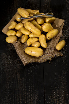 Raw Cherie potatoes and peeler on brown paper, jute and dark wood