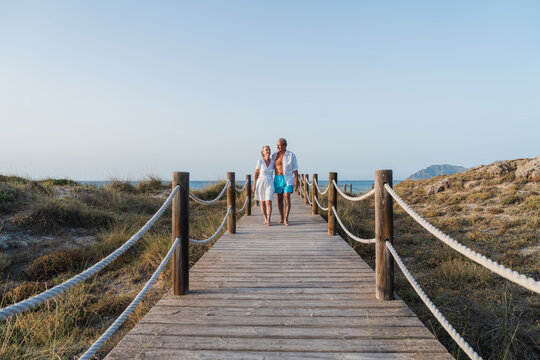 Senior couple walks on a wooden boardwalk near the ocean
