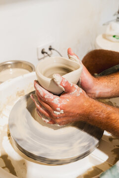 Male potter shapes wet clay on a spinning wheel in a workshop