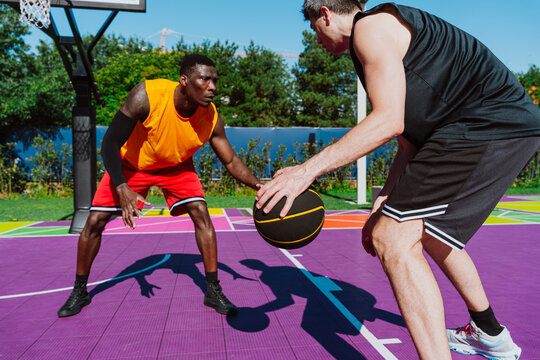 Men play a competitive streetball game on a colorful outdoor court