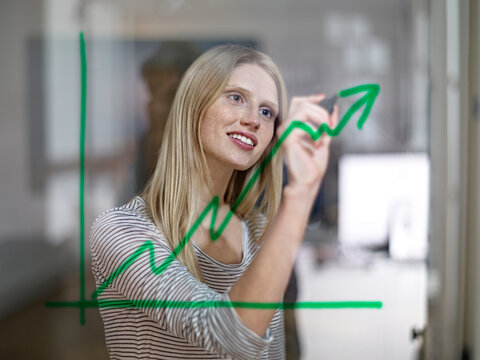Businesswoman draws a growth graph on a glass window in the office