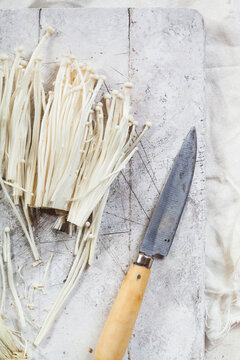 Enoki mushrooms and kitchen knife on wood