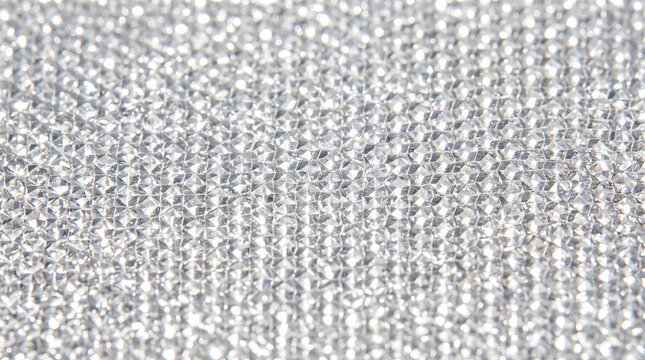 Macro view showing shiny silver metallic textured surface featuring thousands of tiny repeating geometric hexagonal prisms reflecting bright intense sunlight