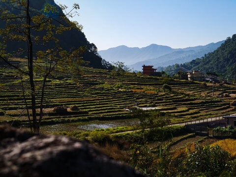 Scenic view of terraced rice fields in a rural mountain valley with distant village and mountains