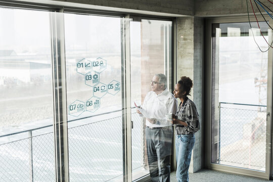 Businessman and woman at windowpane with data in office