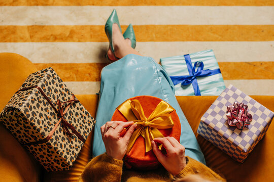 Woman unwraps a colorful gift box while sitting on a yellow sofa